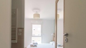 A modern hotel room with a bed, a window, and a mirror.