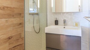 A modern bathroom with a glass shower enclosure, a white sink, and a stainless steel cabinet.