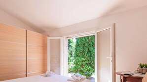 A bedroom with a bed, a wooden wardrobe, and a view of greenery through an open door.