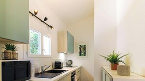 A modern kitchen with a black countertop, a sink, a coffee maker, and a stove. There are two windows providing natural light, and a wall-mounted light fixture above the counter.