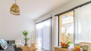 A living room with a sofa, a coffee table, a hanging light, a plant, and a breakfast setup with fruit and drinks.