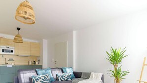 A modern apartment with a grey sofa, wooden dining table, and a kitchen area.