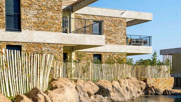 A modern multi-story building with stone facade and balconies overlooking a body of water.
