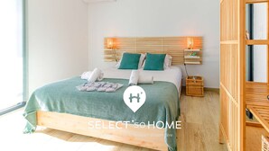 A bedroom with a bed, two pillows, a bedside table, a lamp, and a window.