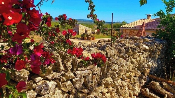 A stone wall with red flowers, a stone building, and a clear blue sky. - Charming 2-bedroom villa in Santa Margalida with AC, WiFi, fitness room (Santa Margalida)