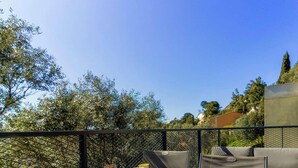 A balcony with outdoor furniture, a stone wall, and a view of trees and buildings. - Bright apartment with terraces, pool in secure domain (Bormes-les-Mimosas)