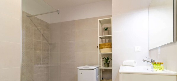 A bathroom with a shower, a toilet, a sink with toiletries, and a shelf with a plant and baskets. - Bright apartment with terraces, pool in secure domain (Bormes-les-Mimosas)