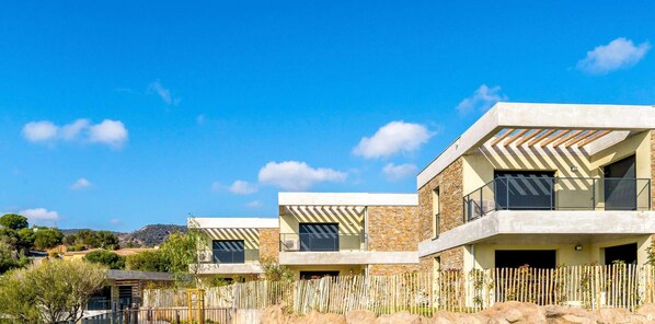 Un edificio residencial moderno de varios pisos con fachada de piedra, ventanas amplias y un balcón.