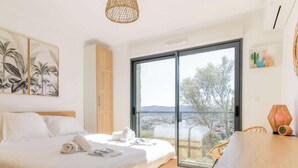 A bedroom with a bed, a large window, and a view of the outdoors. - Bright apartment with terraces, pool in secure domain (Bormes-les-Mimosas)