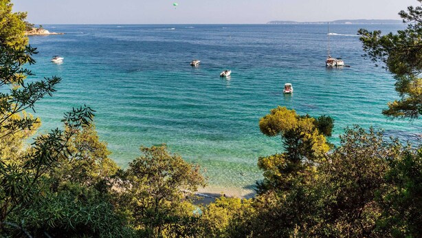 A coastal view with clear turquoise waters, boats, and dense green foliage. - Bright apartment with terraces, pool in secure domain (Bormes-les-Mimosas)