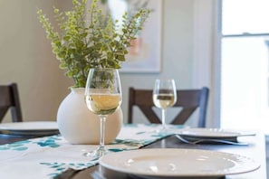 A dining table with two plates, a vase with green foliage, and two glasses of white wine. - Geneva Home w/ Hot Tub, Walk to HWS (Geneva)