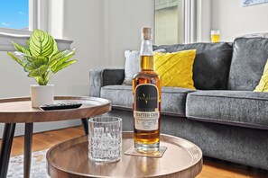 Une bouteille de whisky bourbon CRAFTED CASK, posée sur un dessous de verre, un verre et une télécommande, le tout sur une table ronde en bois.