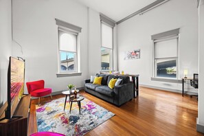Un salon spacieux avec un canapé gris, un fauteuil rouge et un tapis aux couleurs vives.