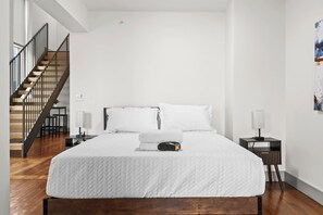 Une chambre à coucher avec un grand lit, un plancher en bois, un escalier et une table de chevet avec une lampe.