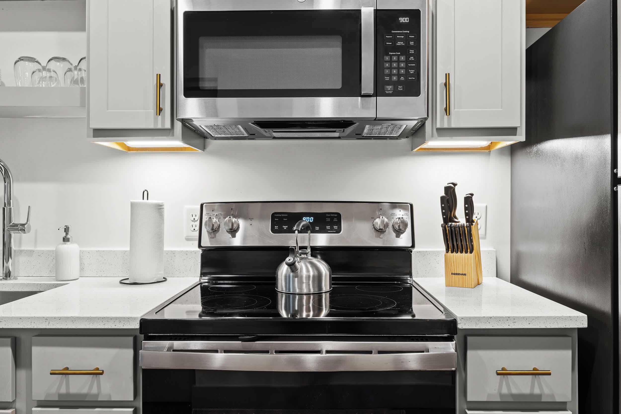 A modern kitchen with stainless steel appliances, including a microwave, oven, and kettle.