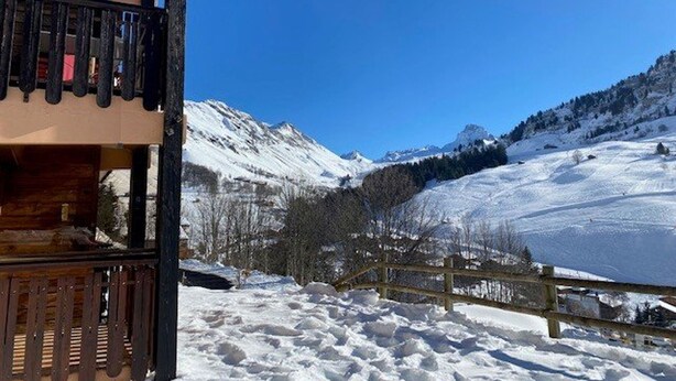 En træhytte med balkon med udsigt over et snøklædt bjerglandskab.