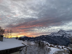 Lumipeitteinen vuoristo, taivaalla auringonlasku ja pilviä.