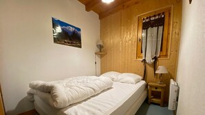Ett sovrum med en säng, ett träfärgat sänggavel, ett nattduksbord med en lampa, ett fönster med gardiner och en tavla som hänger på väggen.