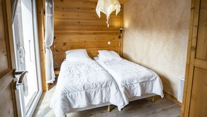 A wooden cabin bedroom with two beds, a hanging light fixture, and a window with curtains.