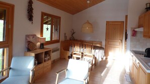 A spacious living area with a high wooden ceiling, a dining table with chairs, a kitchen area with wooden cabinets, and a window with star decorations. - Charming 3-room south with balcony near cable cars, 6 ppl (Le Grand-Bornand)