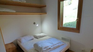 A single bed with white bedding, a bedside lamp, and a window with a view of greenery. - Charming 3-room south with balcony near cable cars, 6 ppl (Le Grand-Bornand)