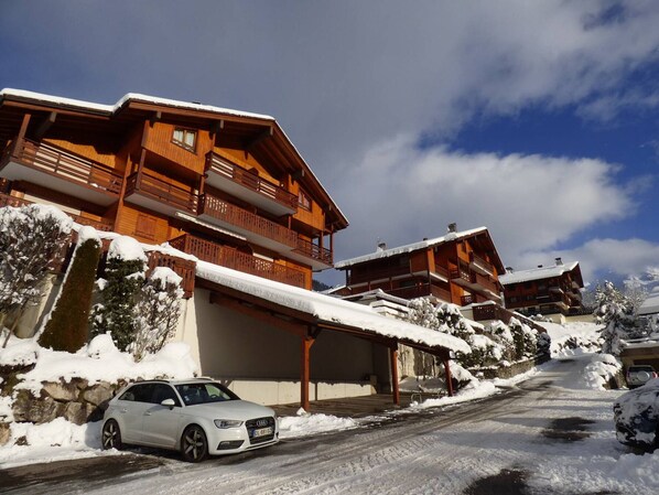 A wooden chalet with balconies, a car parked in front, and snow on the ground.