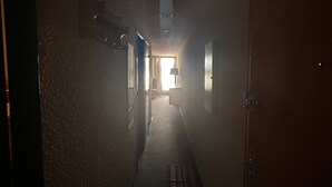 Ein schmaler, schwach beleuchteter Korridor mit Teppichboden, der zu einem Raum mit einer sichtbaren Tür und einem Fenster führt.