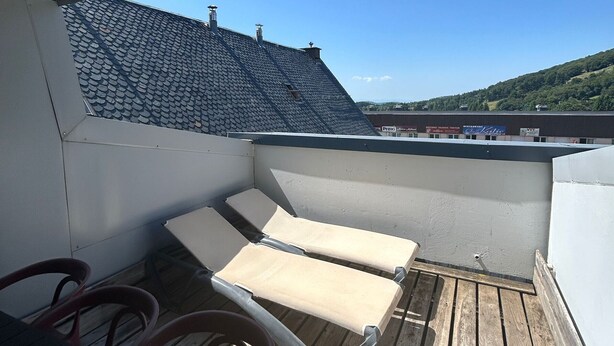 Eine Dachterrasse mit zwei beigen Liegestühlen und einem Holzboden.