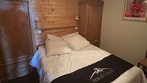 Ein Schlafzimmer mit hölzernem Kopfteil, einem Bett mit weißer Bettwäsche, einer schwarzen Decke mit einem Logo und einem Poster an der Wand.