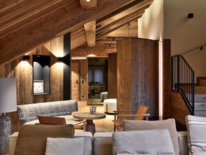 A cozy loft-style room with a high ceiling, wooden beams, a sofa set, a small round table, and a staircase.