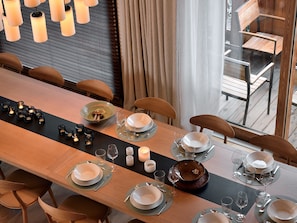 A dining area with a long table set for a meal, chairs around, and a view of the outdoors.