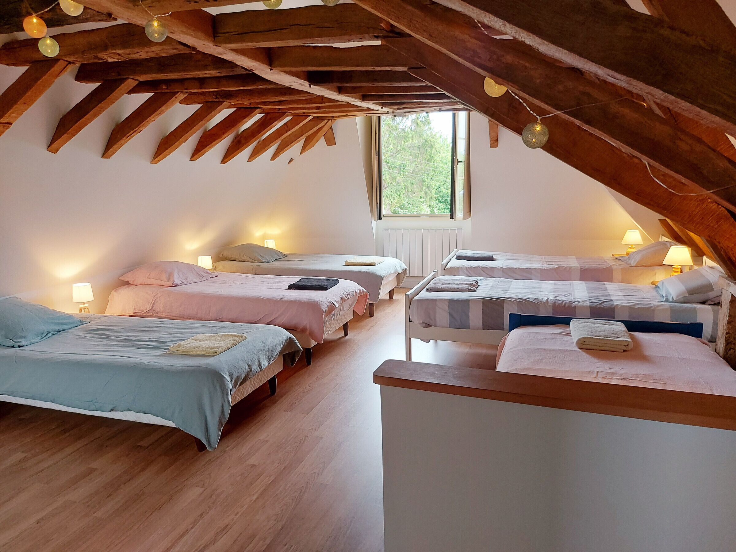 Un dormitorio ático acogedor con cuatro camas dispuestas en fila, vigas de madera y luces colgantes.