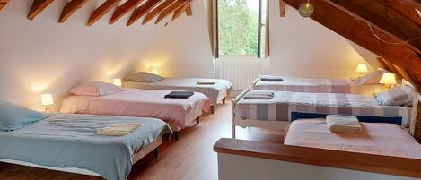 Un dormitorio ático acogedor con cuatro camas dispuestas en fila, vigas de madera y luces colgantes.