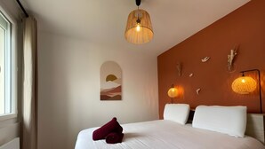 Et hotelværelse med en stor seng, et vindue med gardiner, et billede hængt på væggen og to væglamper.