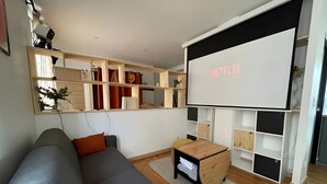 En moderne stue med en grå sofa, et træ sofabord og en stor hvid væg med Netflix logo.