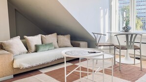 Un salón estilo loft con sofá, mesa de centro y sillas, un ventanal con vistas a edificios y una escalera.