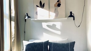 Un dormitorio con cama, almohadas, mesita de noche, lámpara y cuadros en la pared.