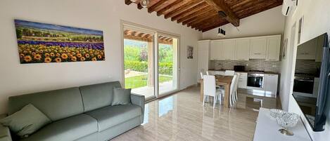 A modern living room with a sofa, a dining area, and a kitchen with white cabinets and stainless steel appliances.
