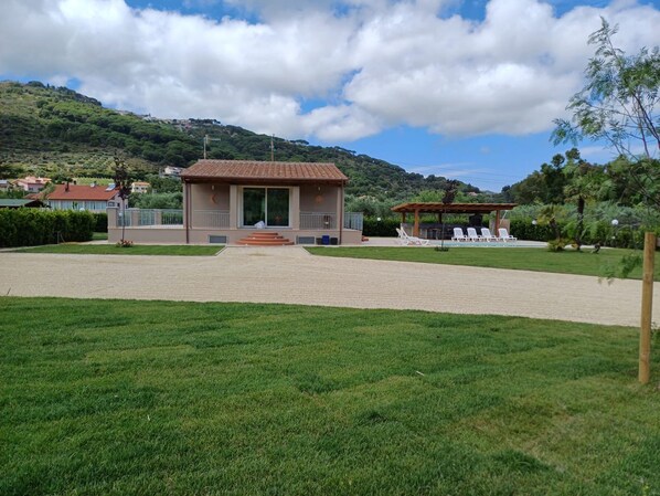 A building with a tiled roof, a paved entrance, and a lawn with outdoor seating.