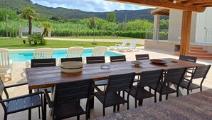 Eine Terrasse im Freien mit Pool, Esstisch und Stühlen, mit Blick auf eine üppige Landschaft und Berge.