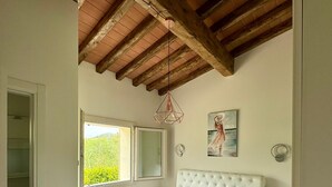Ein Schlafzimmer mit einem großen Bett, einem Fenster, einer Holzbalkendecke und einem Gemälde an der Wand.