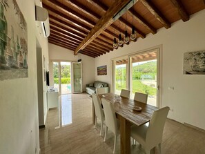 A dining area with a wooden table and chairs, a sofa, and a view of the outdoors through large sliding glass doors.