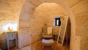 A stone-walled room with a small window, a chair, a wooden stool, a metal rack, and a mirror. - Like Once Upon a Time - The Trullo (with Jacuzzi for exclusive use) 2 km from Alberobello (Martina Franca)