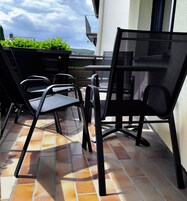 Un patio con dos sillas negras y una mesa, suelo de baldosas y vistas a zonas verdes y colinas al fondo.
