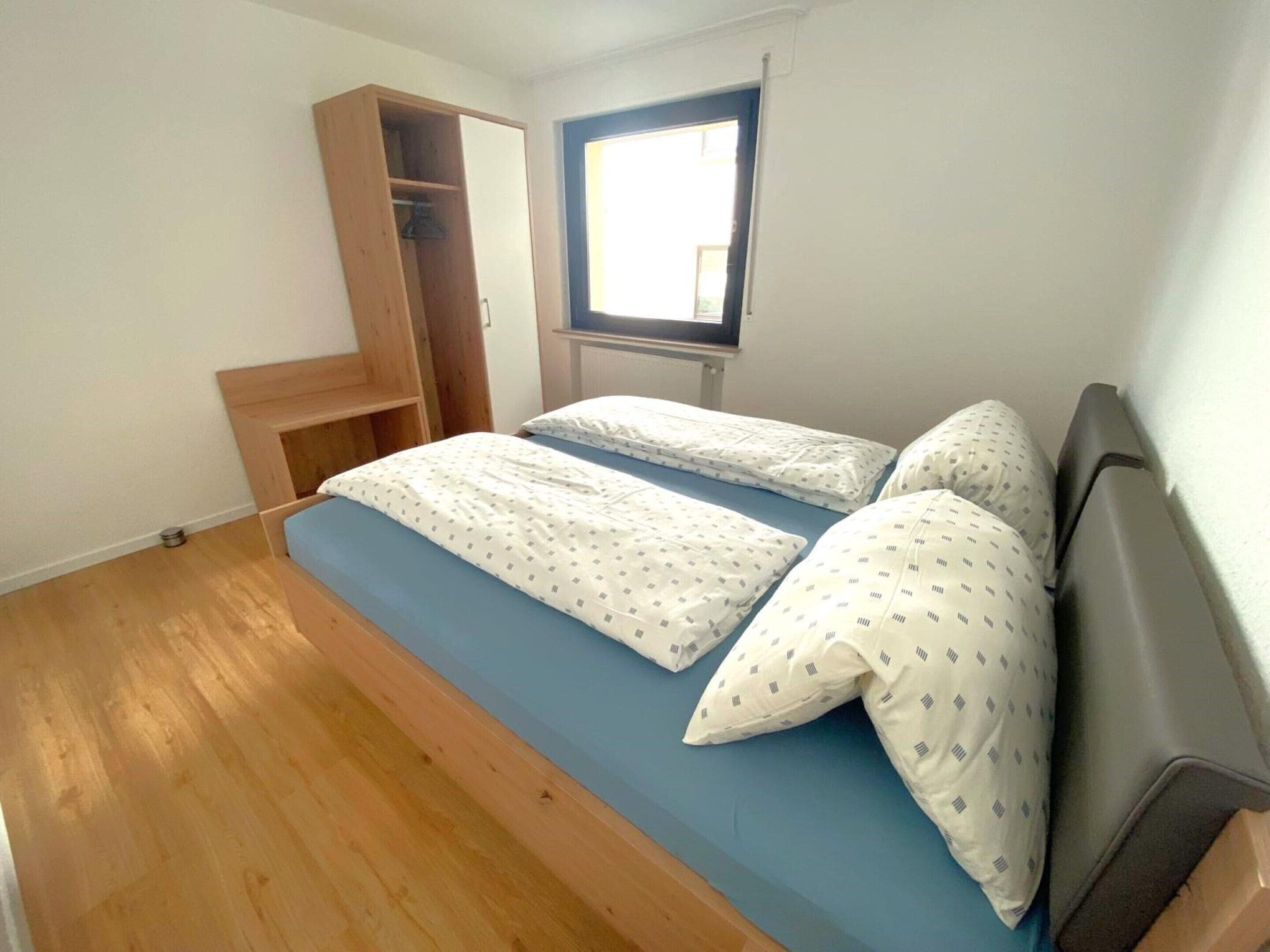 A bedroom with a bed, a wooden wardrobe, and a window.