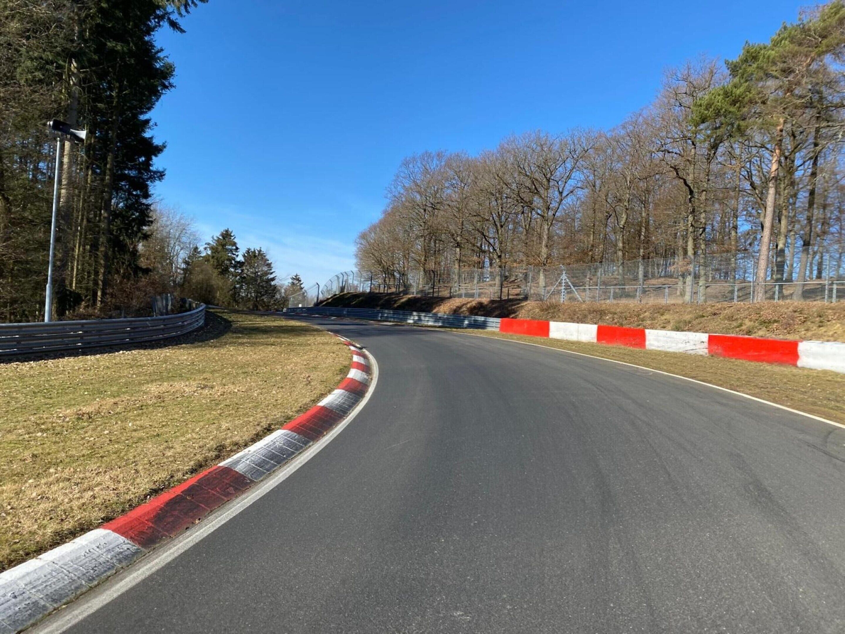 Une piste de course incurvée, bordée de barrières de sécurité et avec des arbres en arrière-plan.