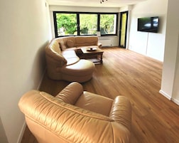 Una sala de estar moderna con un sofá de cuero, una mesa de centro de madera y un televisor montado en la pared.