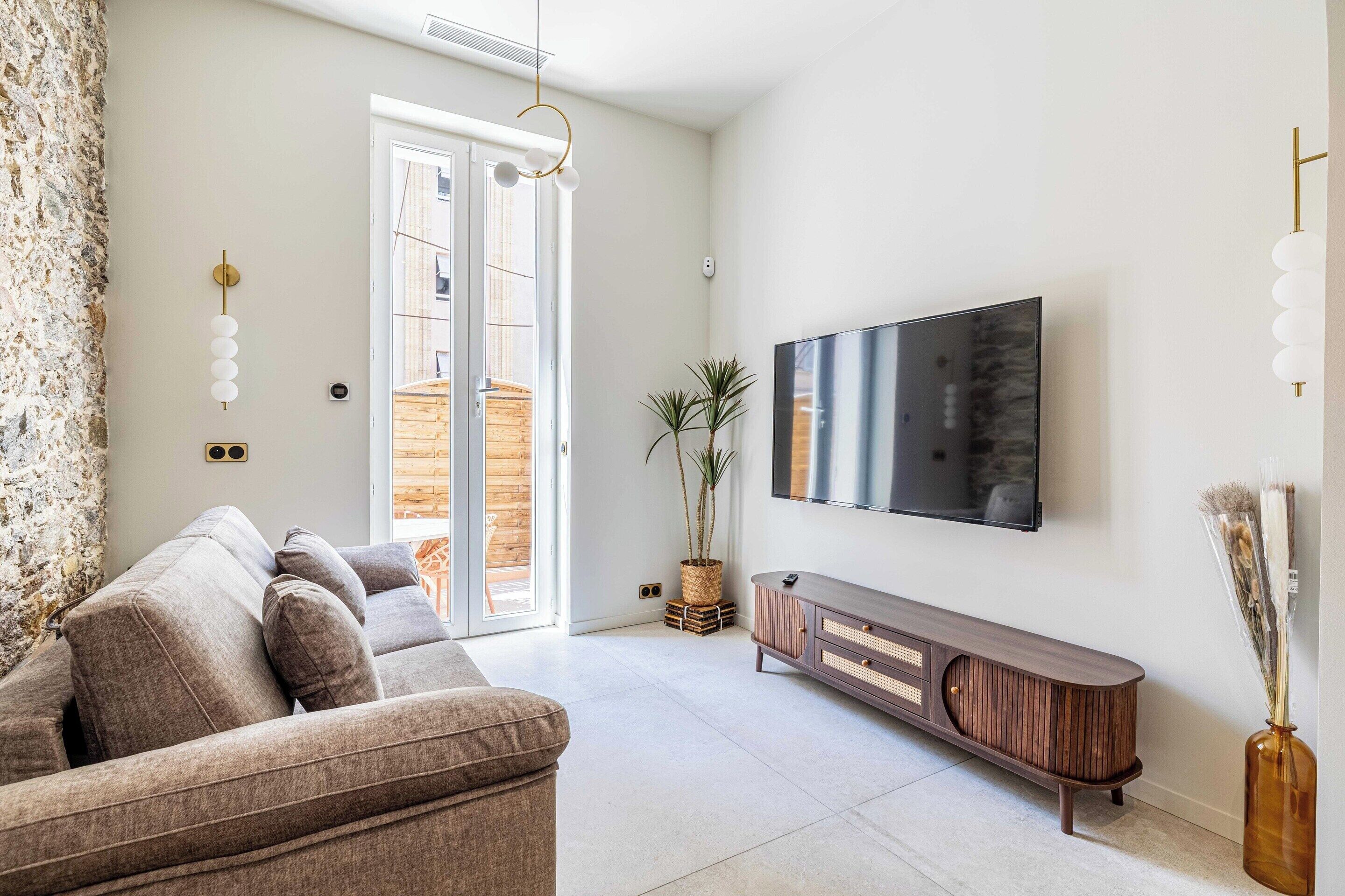 Una sala de estar moderna con un sofá, un mueble de madera, un televisor de pantalla plana y una planta en maceta.