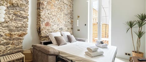 A bedroom with a stone wall, a bed with pillows, a bedside table, and a plant.
