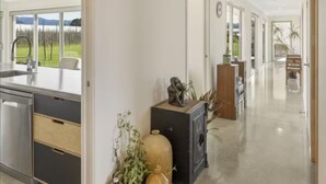 A modern kitchen with a large island, a dining area with a bench, and a view of a green landscape through large windows. - Relax in Riwaka, Sun, Space, Cycle (Riwaka)